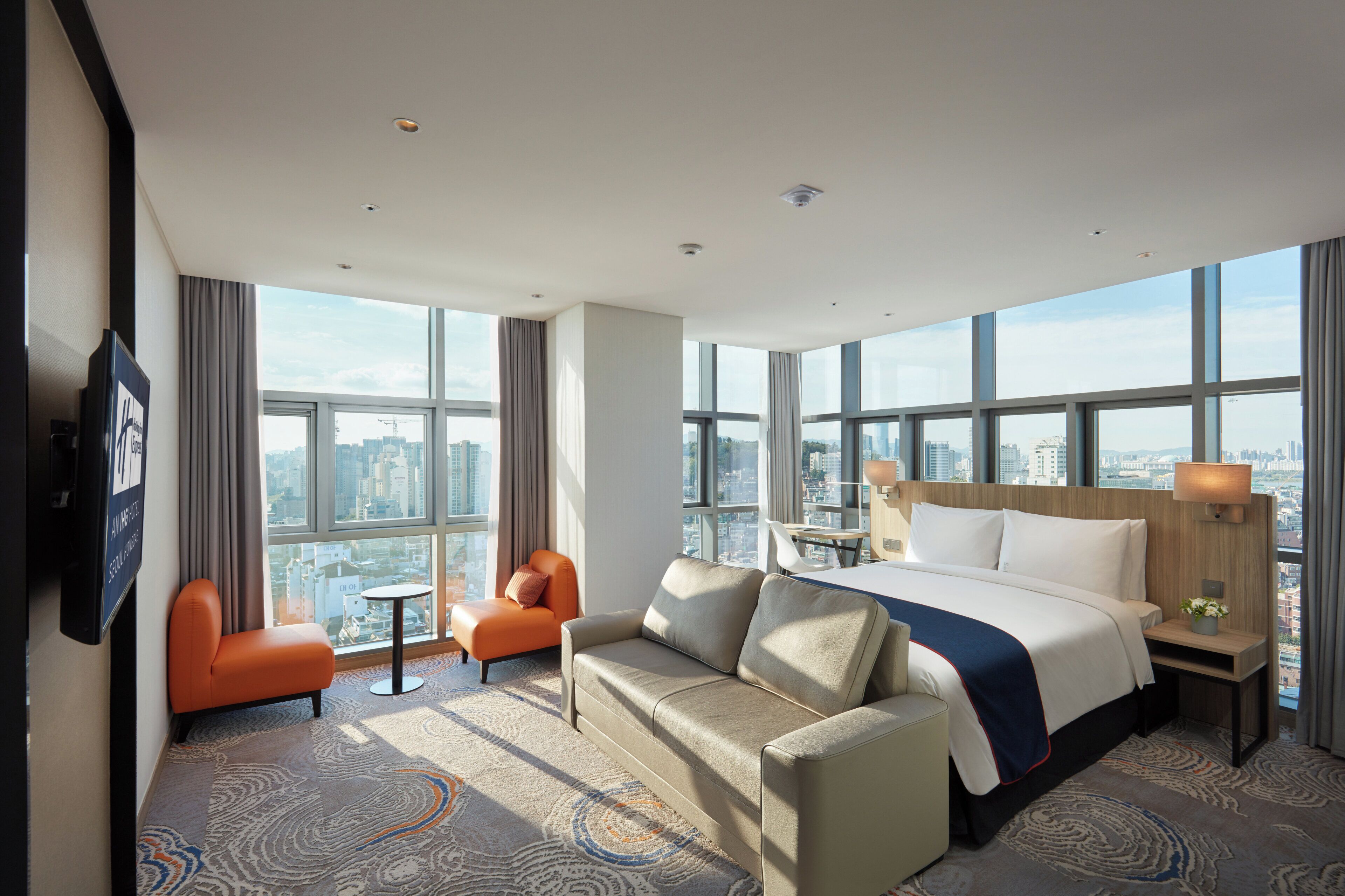 A hotel room with a large bed, a sofa, a chair, a small table, and a TV.
