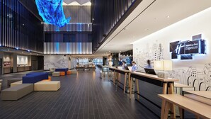 A modern hotel lobby with a reception desk, seating areas, and a large digital display.