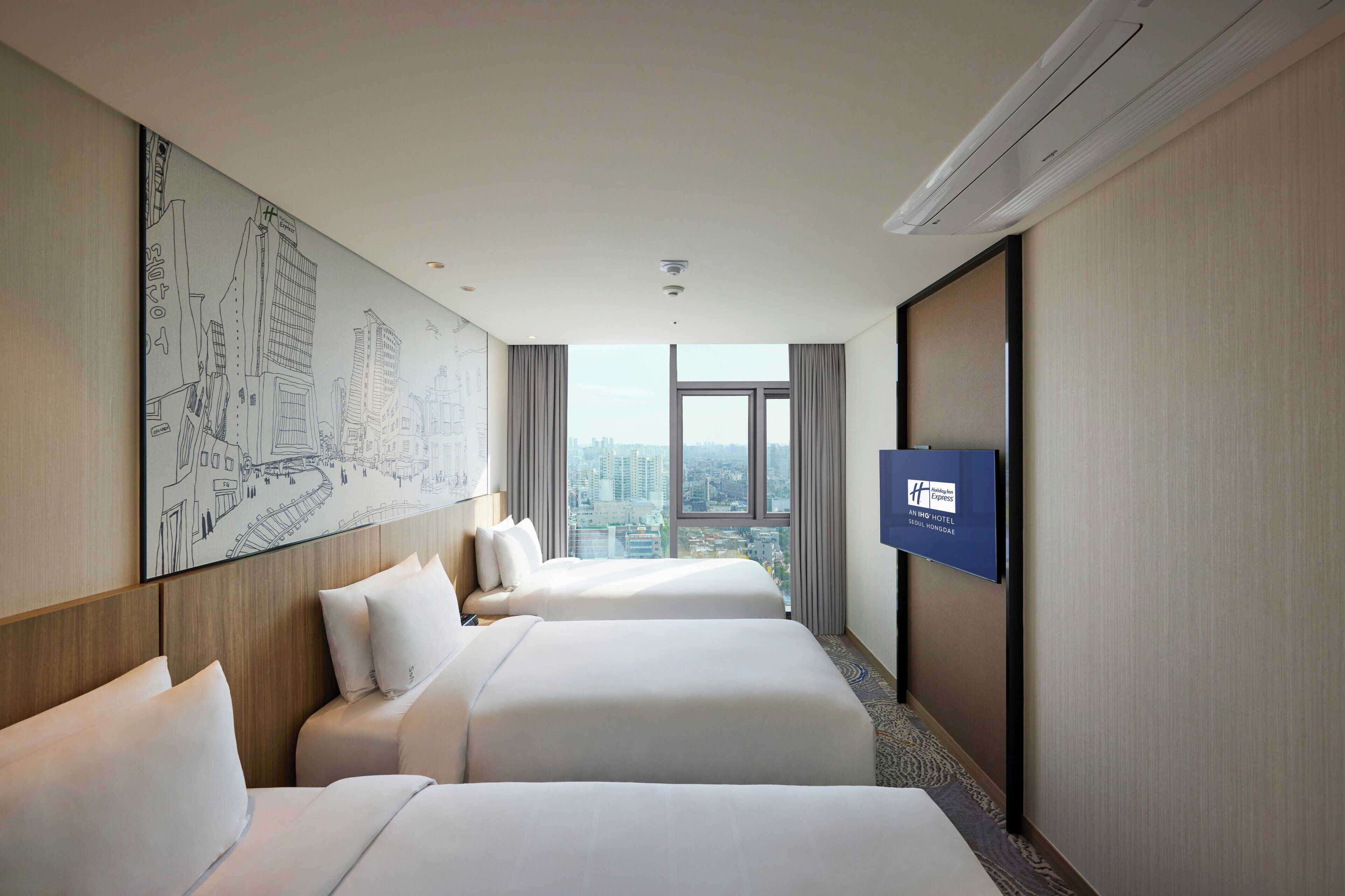 A hotel room with two beds, a large window with a city view, a mounted TV, and a wall-mounted artwork.