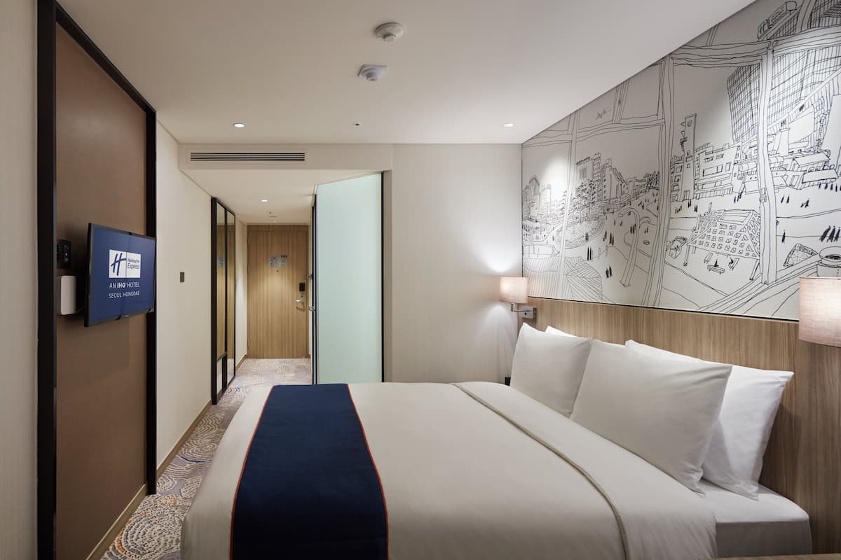 A hotel room with a bed, a TV, a map on the wall, and a door leading to another room.