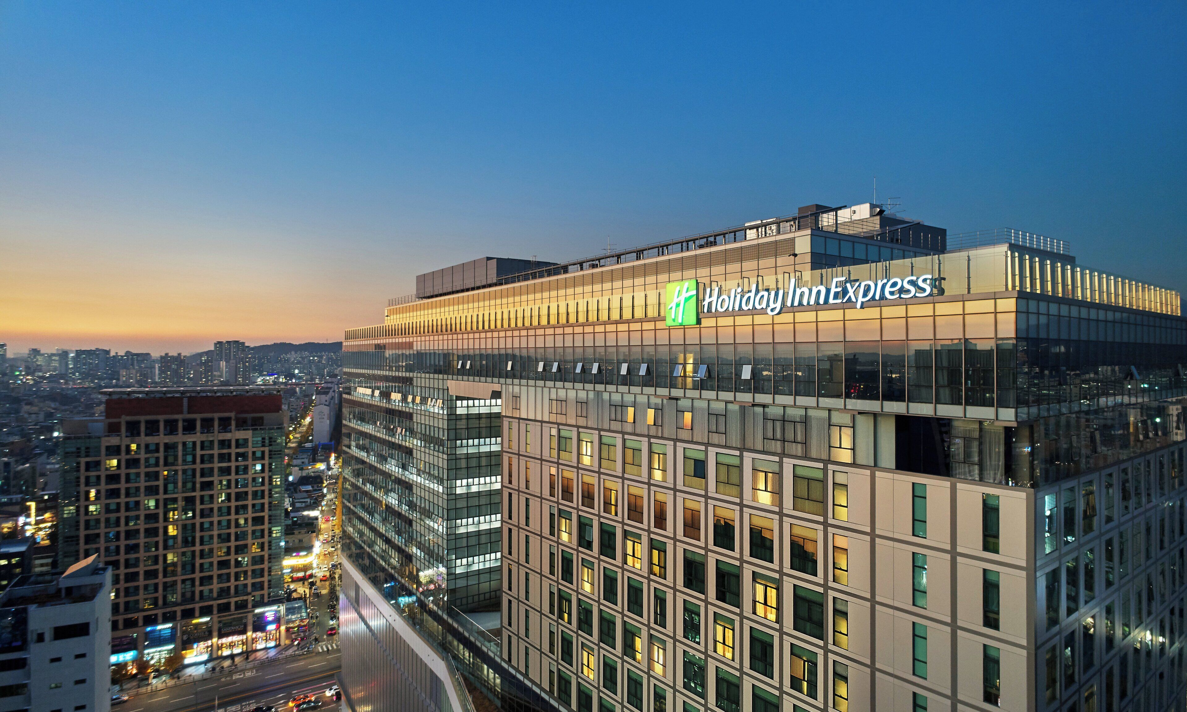 Ein Holiday Inn Express Hotel mit moderner Glasfassade, eingebettet in eine Stadtansicht im Abenddämmerung.