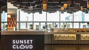 A modern hotel lobby with a 'Sunset Cloud' sign, a reception desk, and a view of the cityscape through large windows.