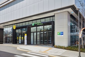 A Holiday Inn Express building with a modern glass facade, a visible entrance with automatic sliding doors, and a clear sky above. - Holiday Inn Express Seoul Hongdae by IHG (Seoul)