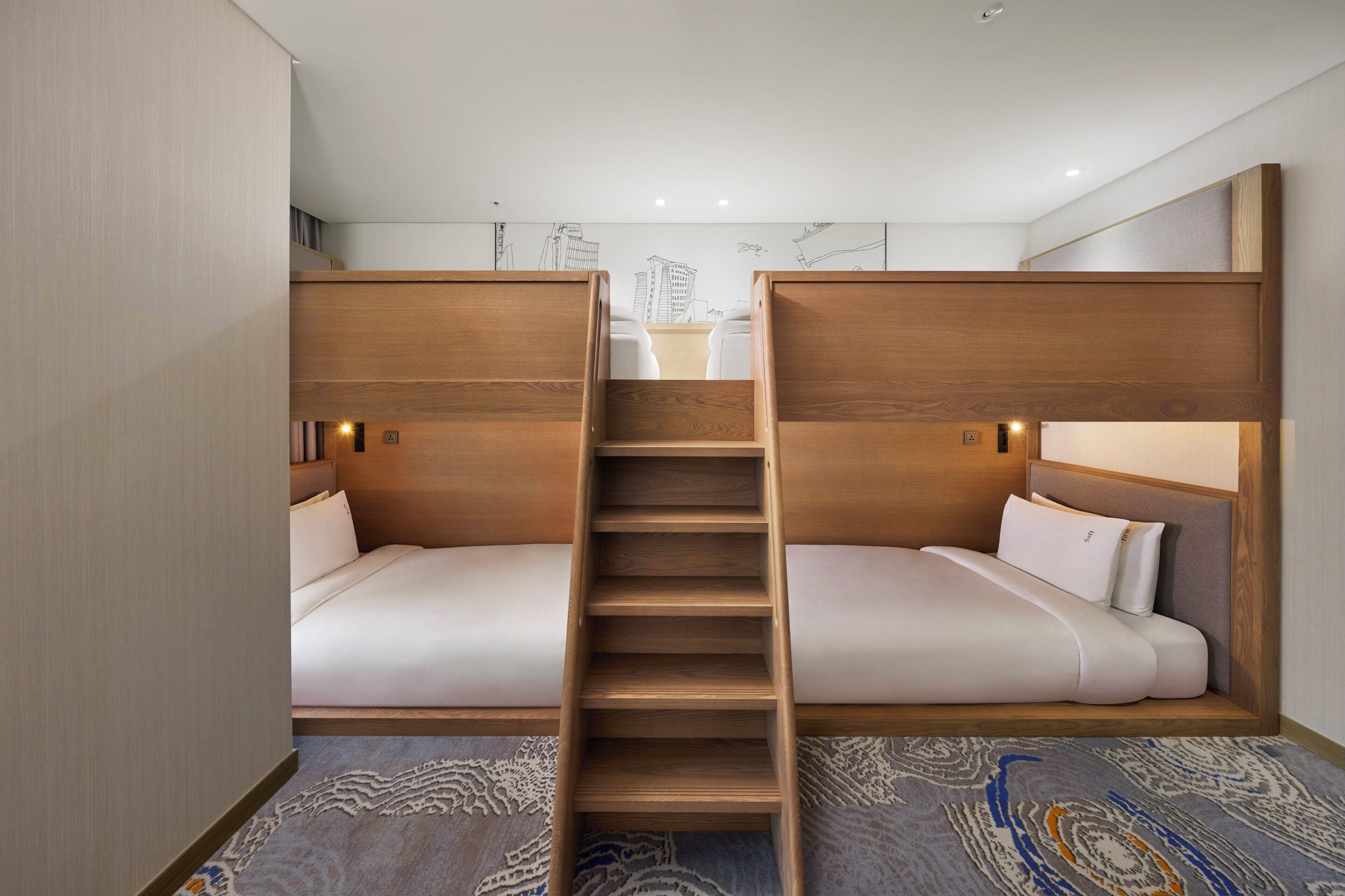 A compact hotel room with two bunk beds, a wooden staircase, and a patterned carpet.