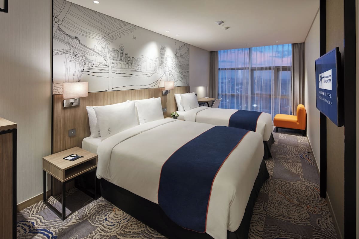 A hotel room with two beds, a large wall mural, a TV, and a city view.