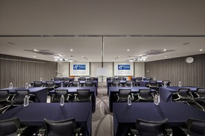 Een vergaderruimte met meerdere tafels en stoelen, waterflesjes op elk tafel, en een klok aan de muur.
