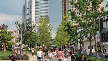 A busy urban street with pedestrians, trees, and modern buildings.