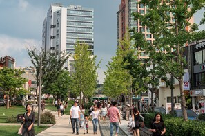 Een levendige stadsstraat met voetgangers, bomen en moderne gebouwen.