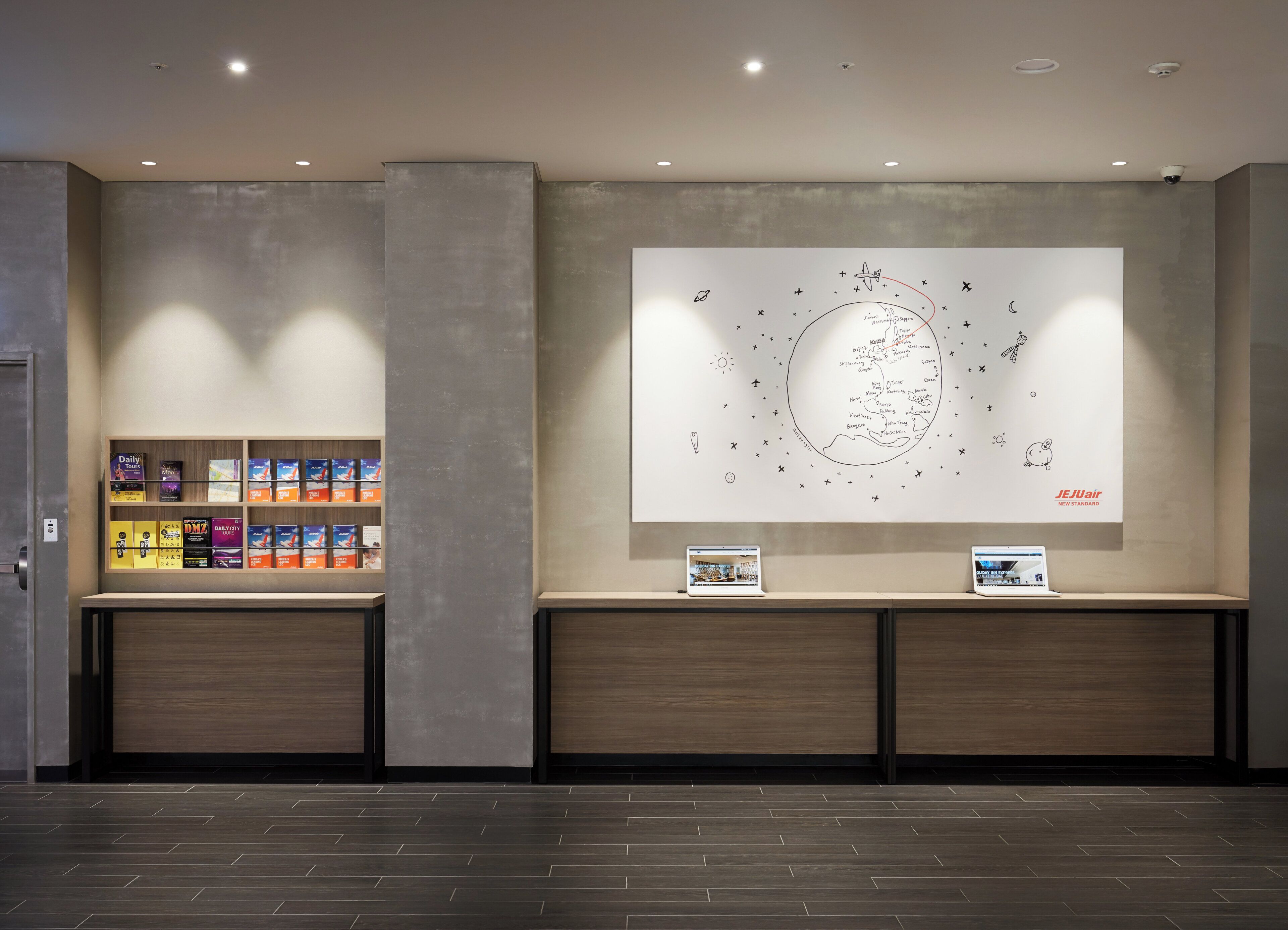 A reception area with a wall-mounted display of travel destinations and a laptop on a counter.