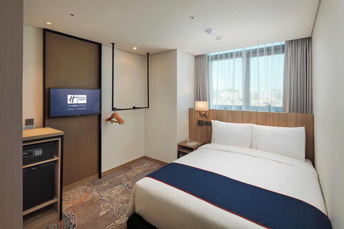 Een hotelkamer met een bed, een televisie, een bureau en een raam met gordijnen.