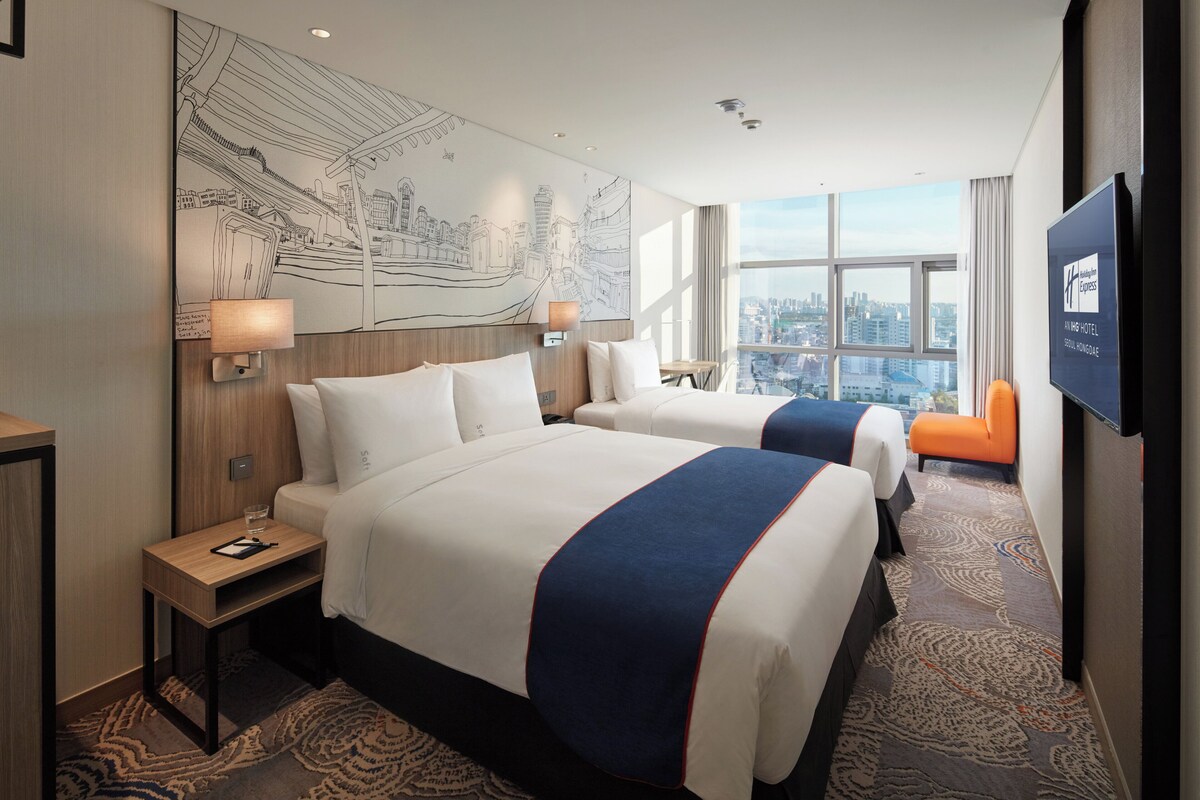 Een hotelkamer met twee bedden, uitzicht op de stad, een groot muurschildering en een televisie.