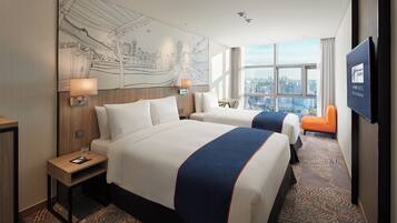 A hotel room with two beds, a cityscape view, a large wall mural, and a television.