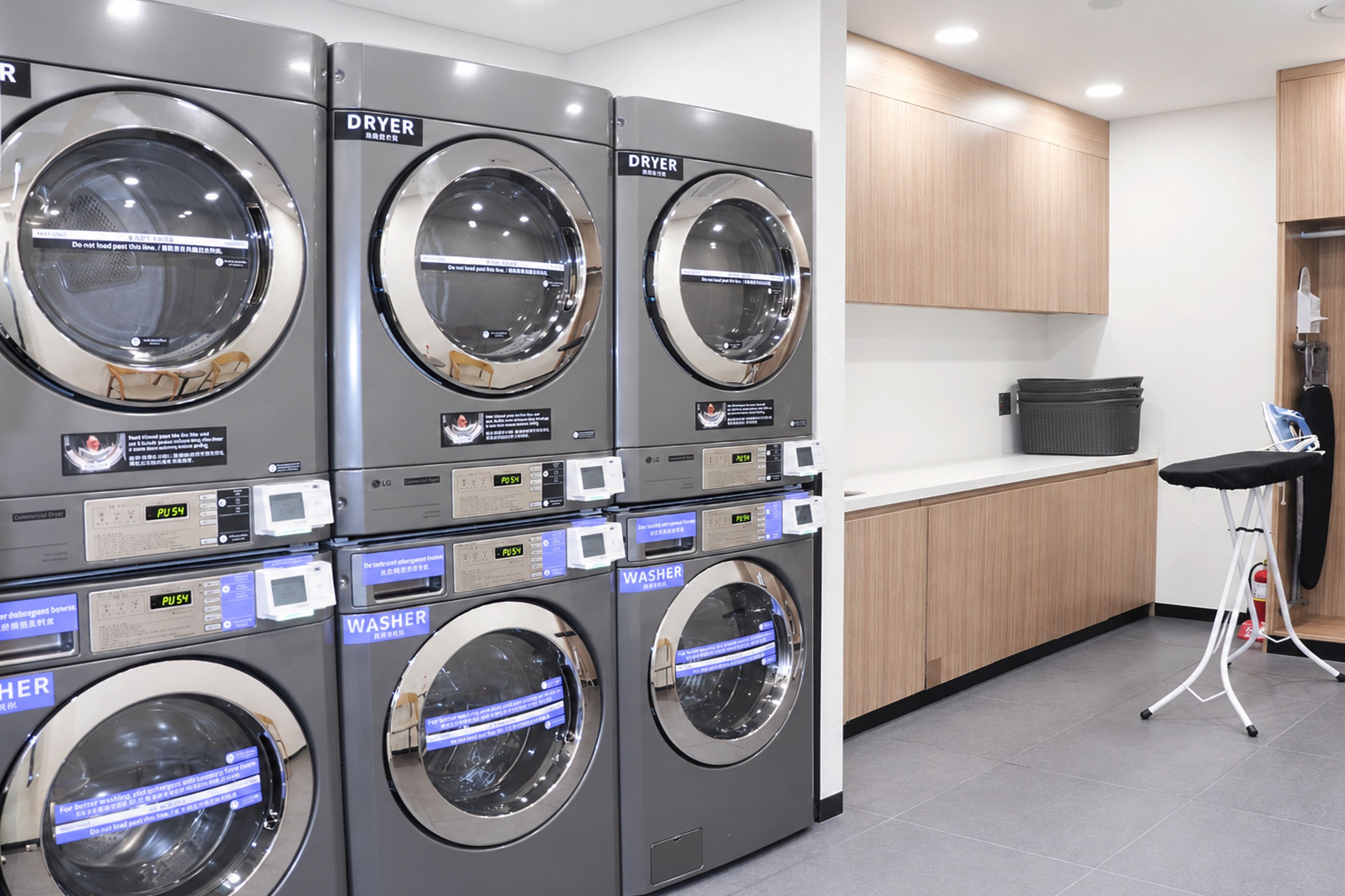 A laundry facility with multiple washing machines and dryers, a small kitchenette area, and a stool for ironing.