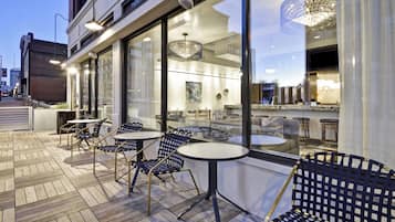 An outdoor seating area with tables and chairs, a glass storefront, and a chandelier.