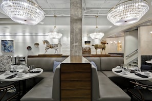 A modern restaurant interior with high ceilings, chandeliers, and unique wall-mounted animal sculptures.