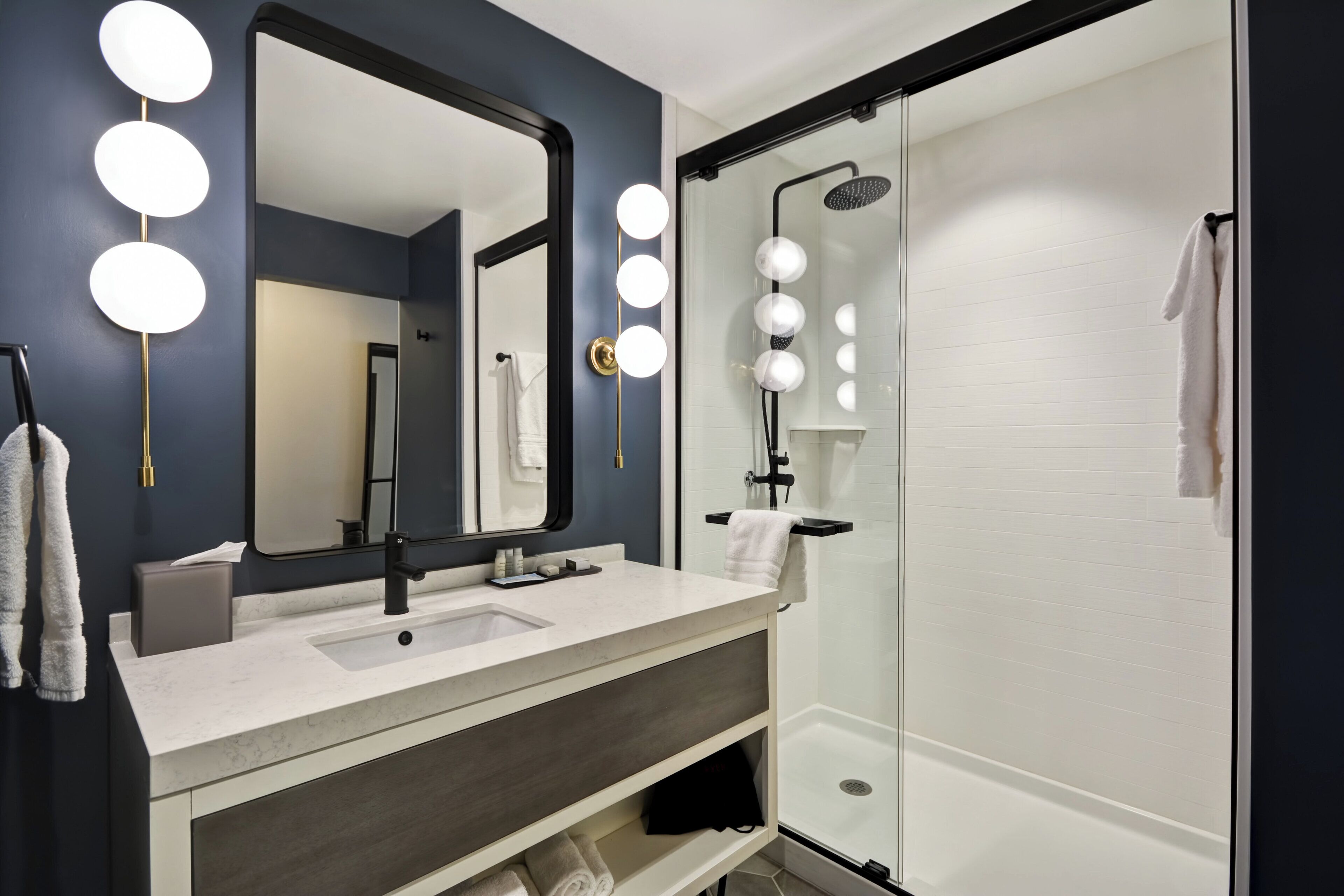 A modern bathroom with a large mirror, vanity, and a glass-enclosed shower.