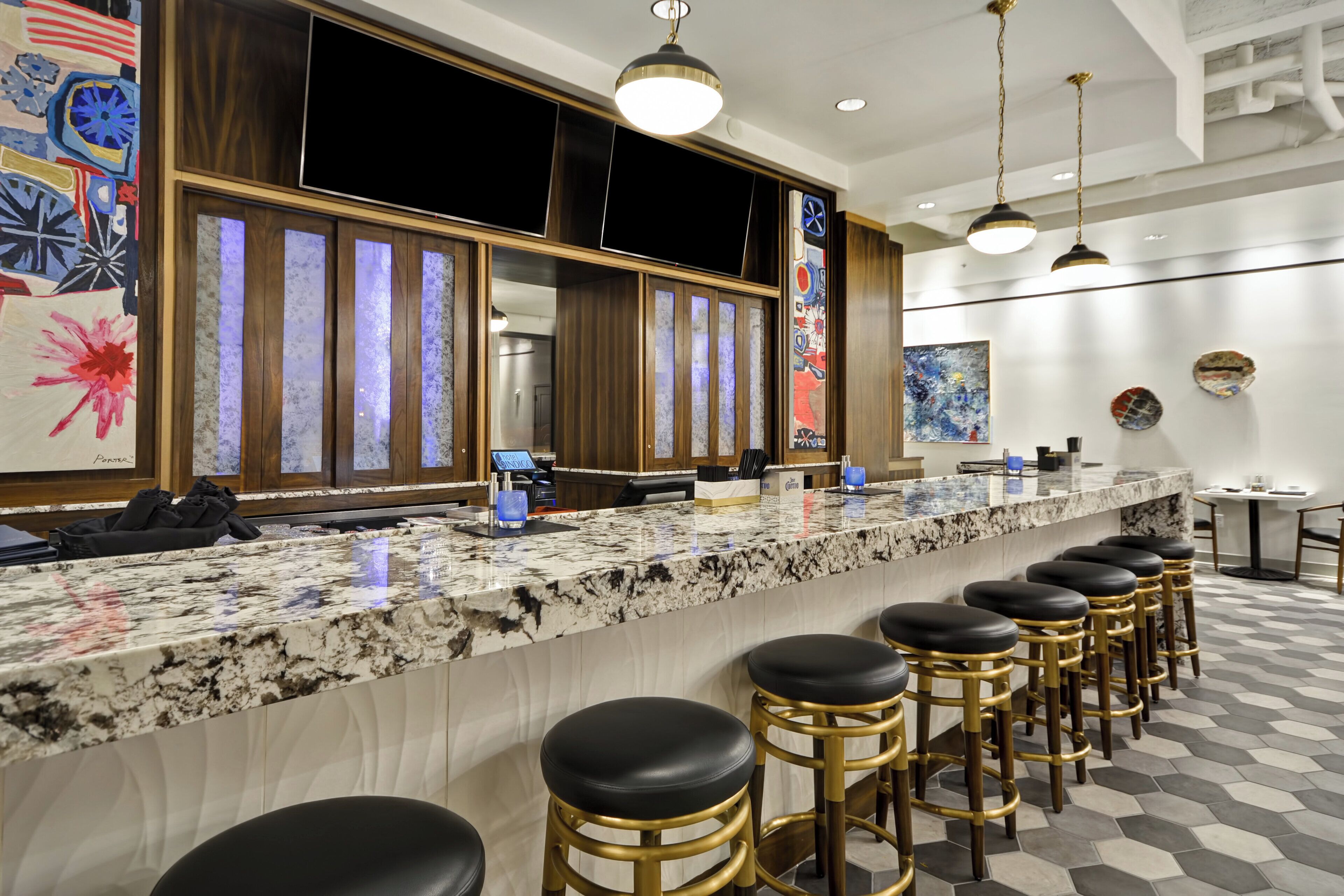 Un bar d’hôtel doté d’un comptoir en marbre, de tabourets noirs et d’un lustre moderne.
