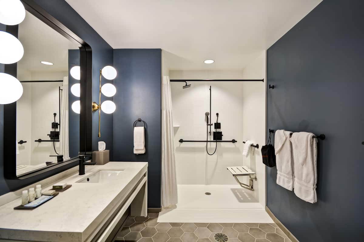 Une salle de bain moderne dotée d’un grand miroir, de deux vasques, d’une zone douche et d’un porte-serviettes.