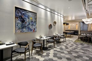 A modern restaurant interior with hexagonal patterned flooring, black leather chairs, white tables, and a large abstract painting on the wall. - Hotel Indigo Kansas City - The Crossroads by IHG (Kansas City)