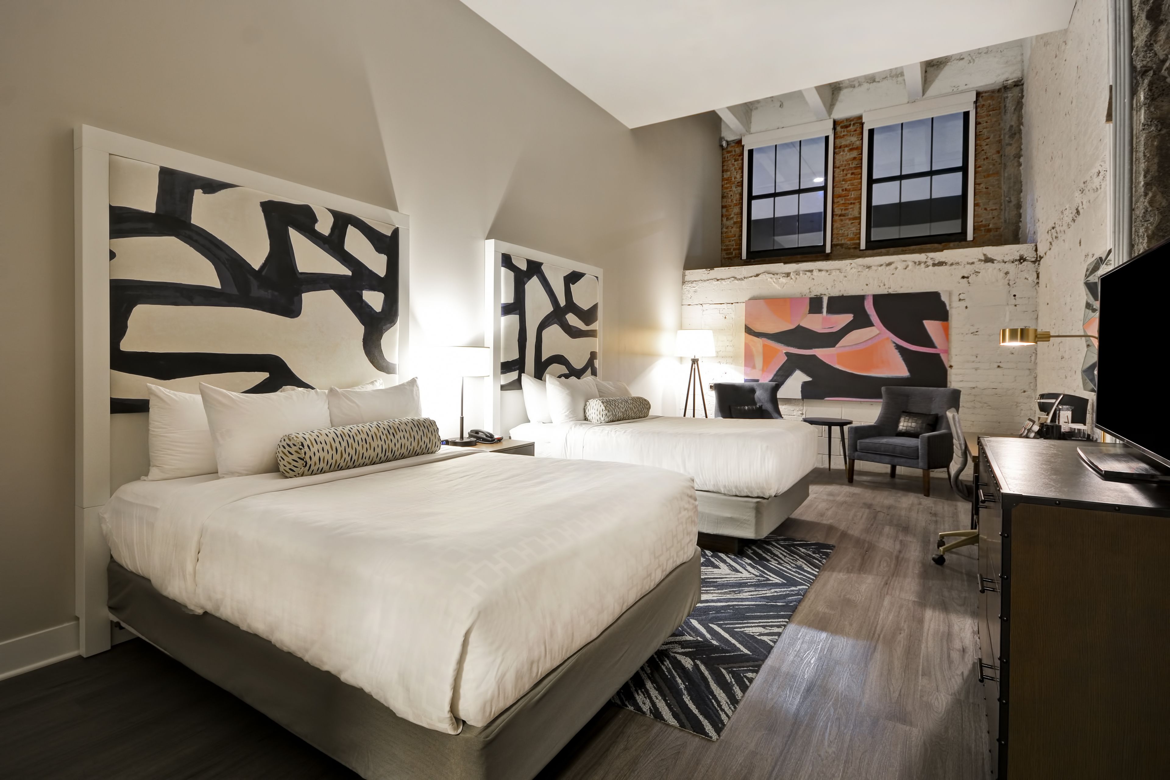 Habitación de hotel con dos camas, un escritorio, una silla y obras de arte en las paredes.
