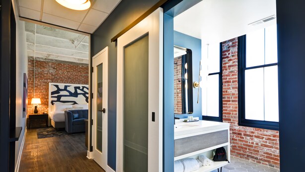 A modern hotel room with a brick wall, a large mirror, a white vanity, and a bed with a headboard. - Hotel Indigo Kansas City - The Crossroads by IHG (Kansas City)
