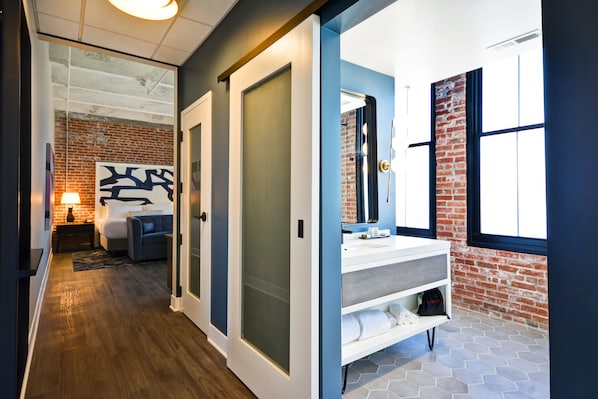 Quarto de hotel moderno com parede de tijolos, um espelho grande, toucador branco e uma cama com cabeceira.