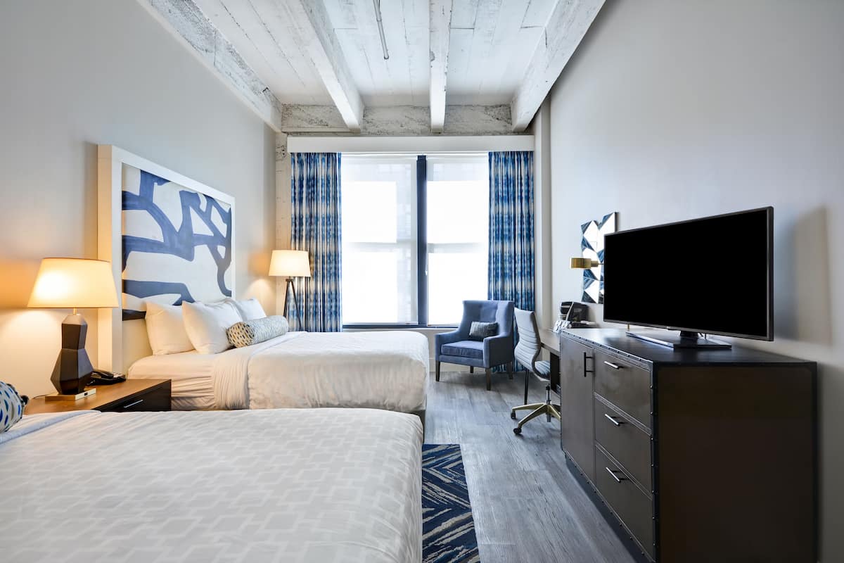 Une chambre d’hôtel avec deux lits, un bureau, une télévision et une grande fenêtre avec des rideaux.