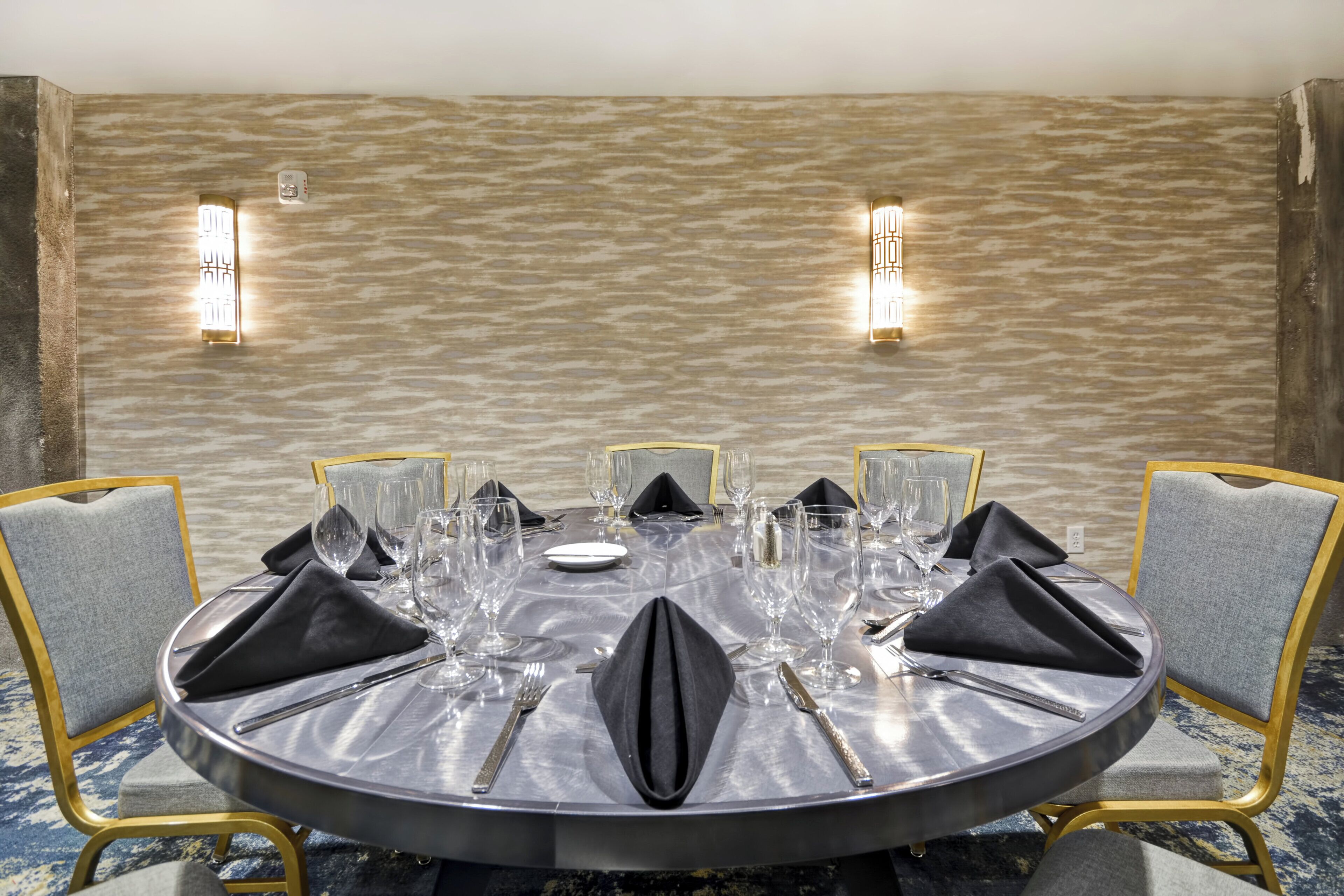 A round dining table with a grey tablecloth, set with multiple wine glasses, plates, and cutlery.