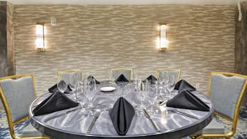 A round dining table with a grey tablecloth, set with multiple wine glasses, plates, and cutlery.