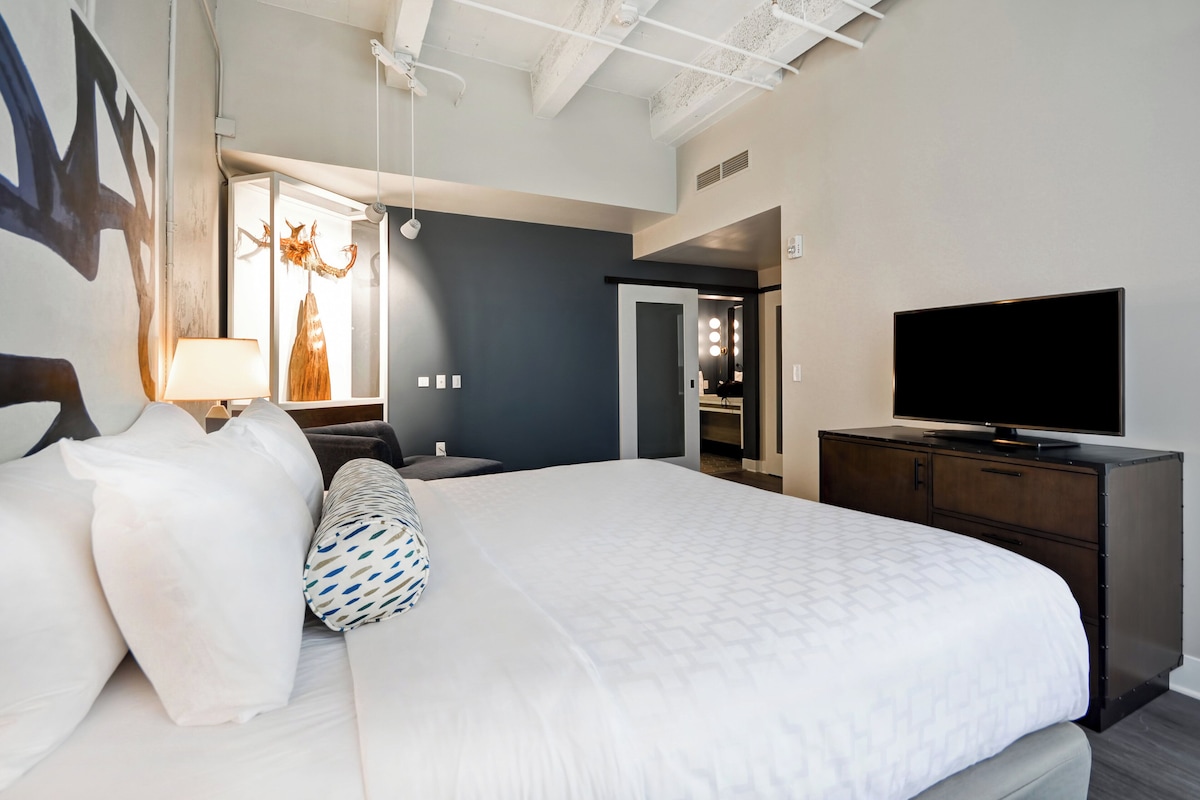 Quarto de hotel moderno com uma cama grande, televisão e guarda-roupa.