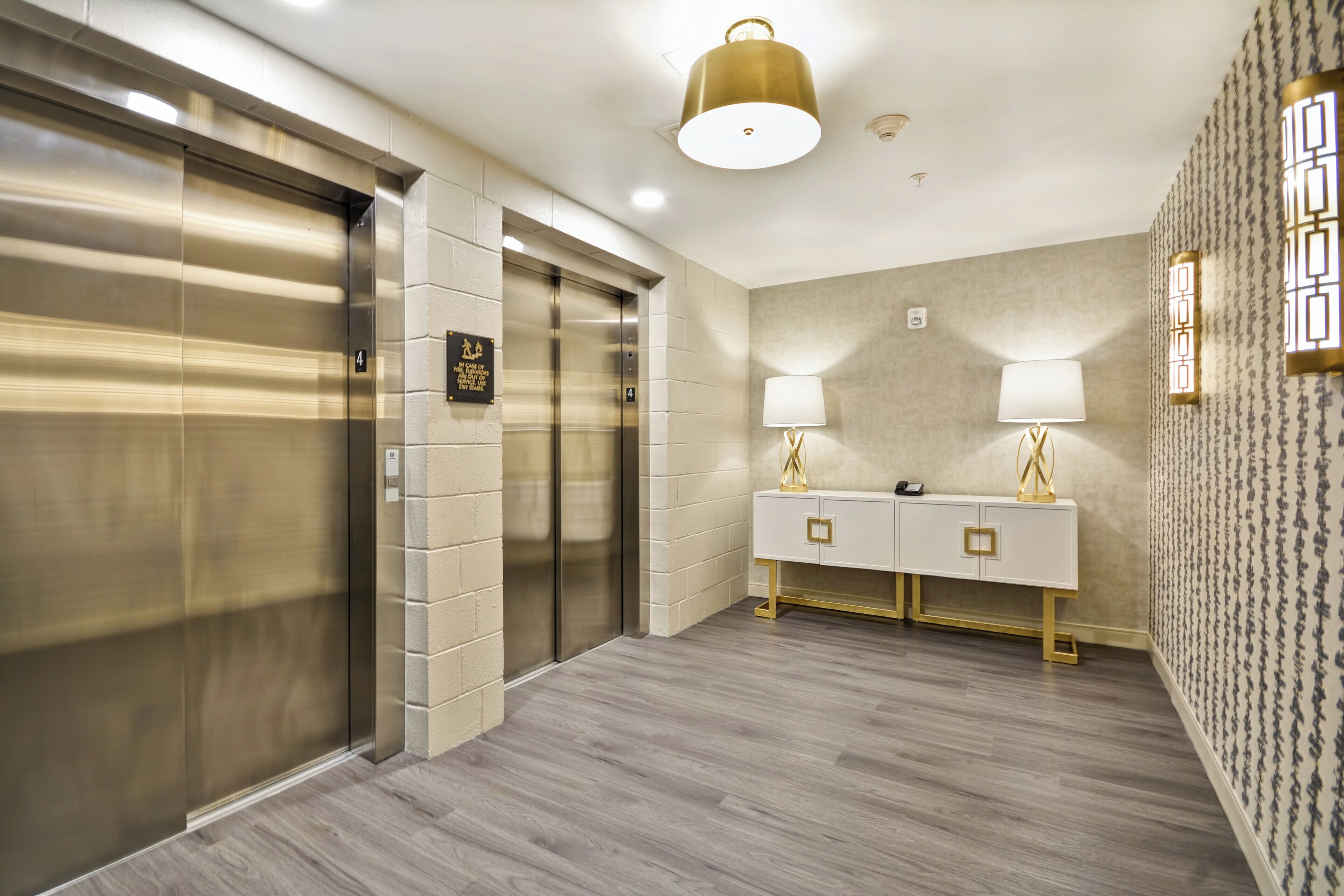A modern elevator with a metallic finish, a wall-mounted sign, and a light fixture above.