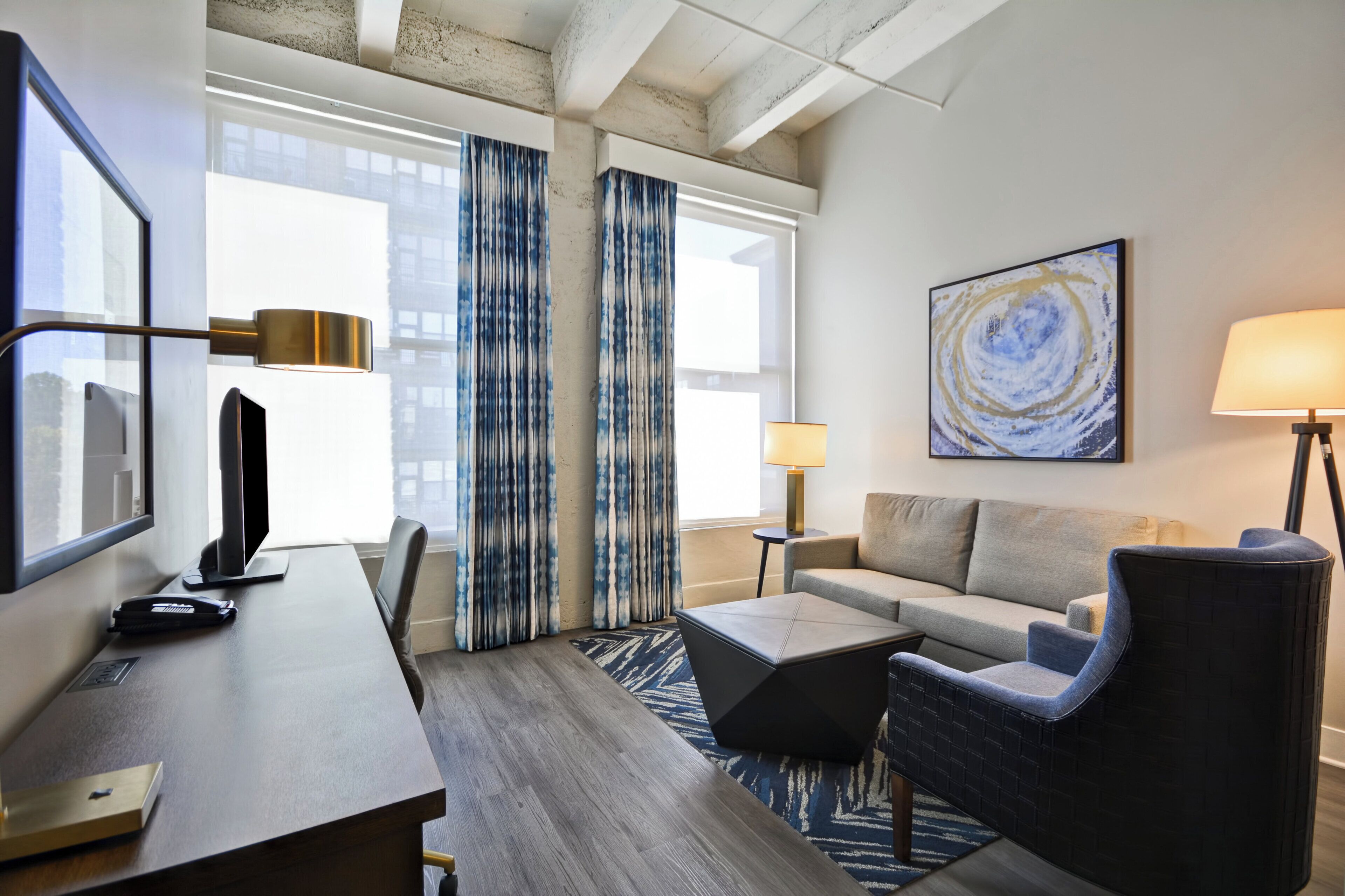 Une chambre d’hôtel équipée d’un bureau, d’une chaise, d’un canapé et d’une grande fenêtre avec des rideaux.