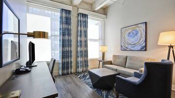 Une chambre d’hôtel équipée d’un bureau, d’une chaise, d’un canapé et d’une grande fenêtre avec des rideaux.