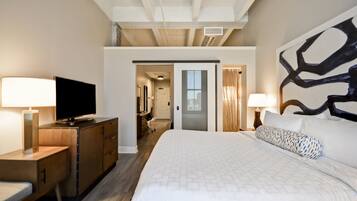 A hotel room with a bed, a desk with a TV, a large abstract painting, and a door leading to a bathroom.