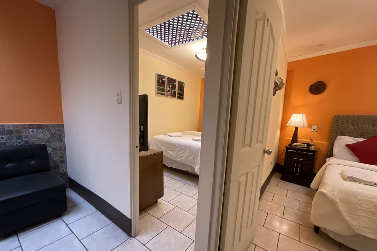 Una habitación de hotel con cama, mesita de noche con lámpara, sofá y ventilador de techo.