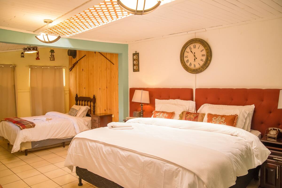 Habitación de hotel con dos camas, un armario de madera, un reloj en la pared y un ventilador de techo.