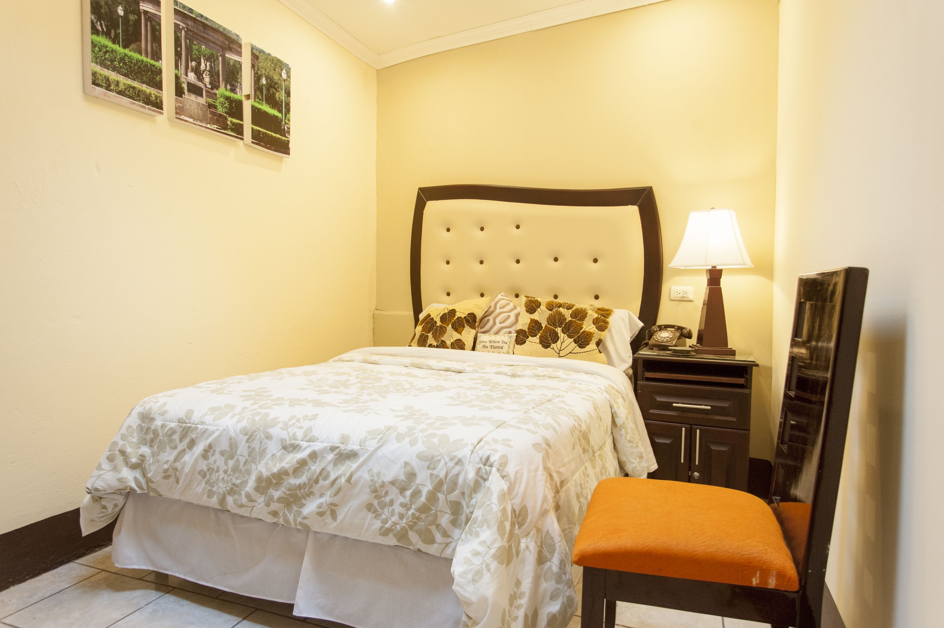 Un dormitorio ordenado con cama, una mesita de noche con lámpara y una silla.