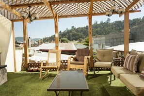 A covered outdoor seating area with wooden furniture and a glass table, overlooking a hilly landscape. - Hotel Vintage Casa las Flores (Quetzaltenango)