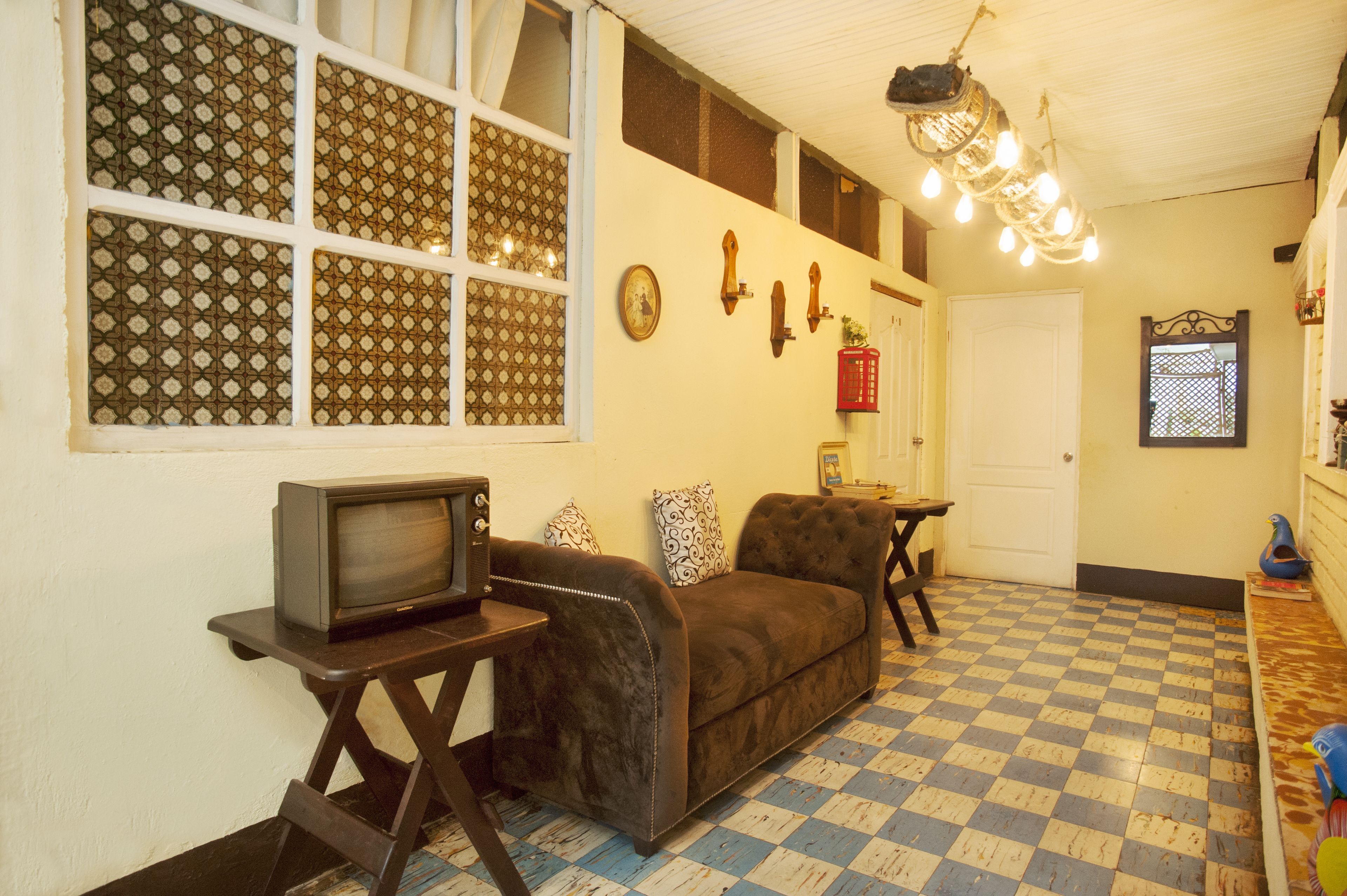 A room with a checkered floor, a brown sofa, a television on a small table, and a chandelier.
