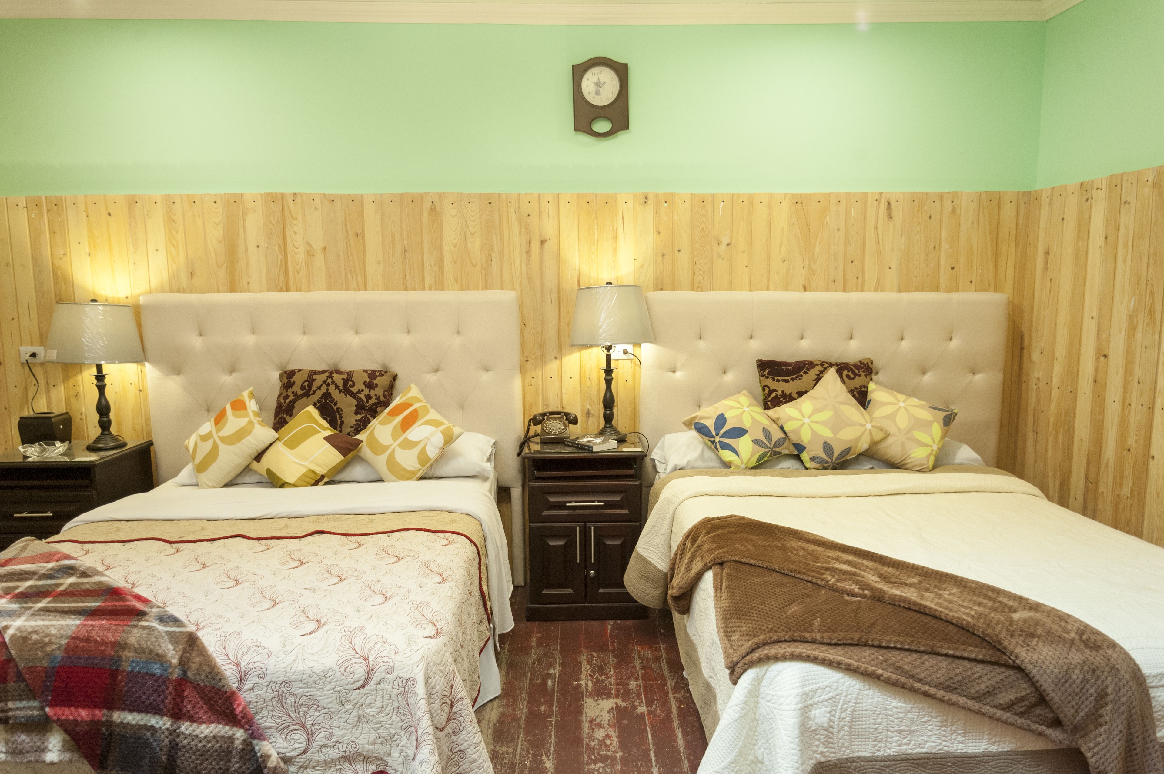 Una habitación con dos camas, paredes de madera panelada, un reloj y lámparas de noche.