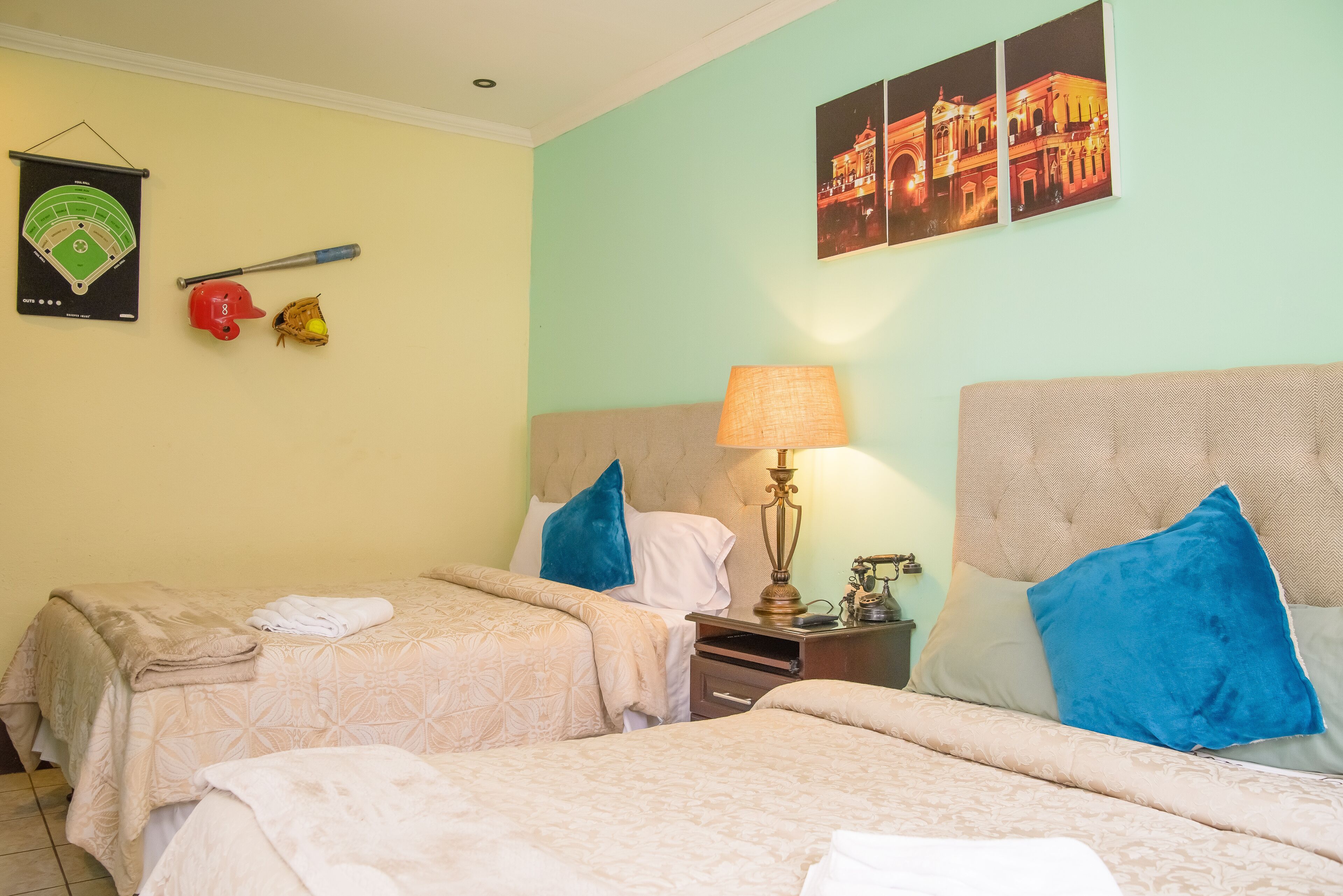 Een hotelkamer met twee bedden, een honkbalknuppel, een handschoen en een ingelijste poster van een honkbalkveld op de muur.