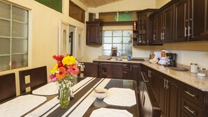 A kitchen with dark wooden cabinets, a granite countertop, and a dining area with a table set for two. - Hotel Vintage Casa las Flores (Quetzaltenango)