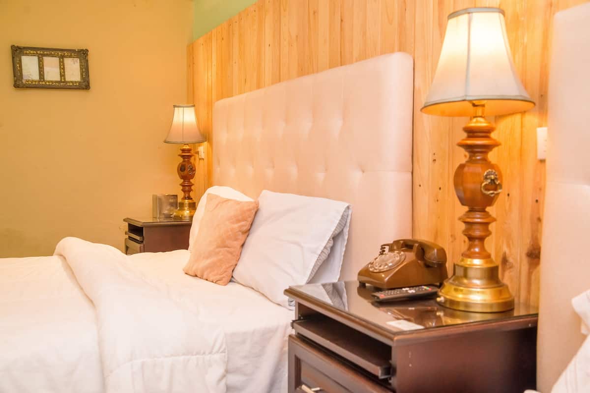 Una habitación de hotel con una cama grande, dos lámparas de noche, un teléfono y un cabecero de madera.