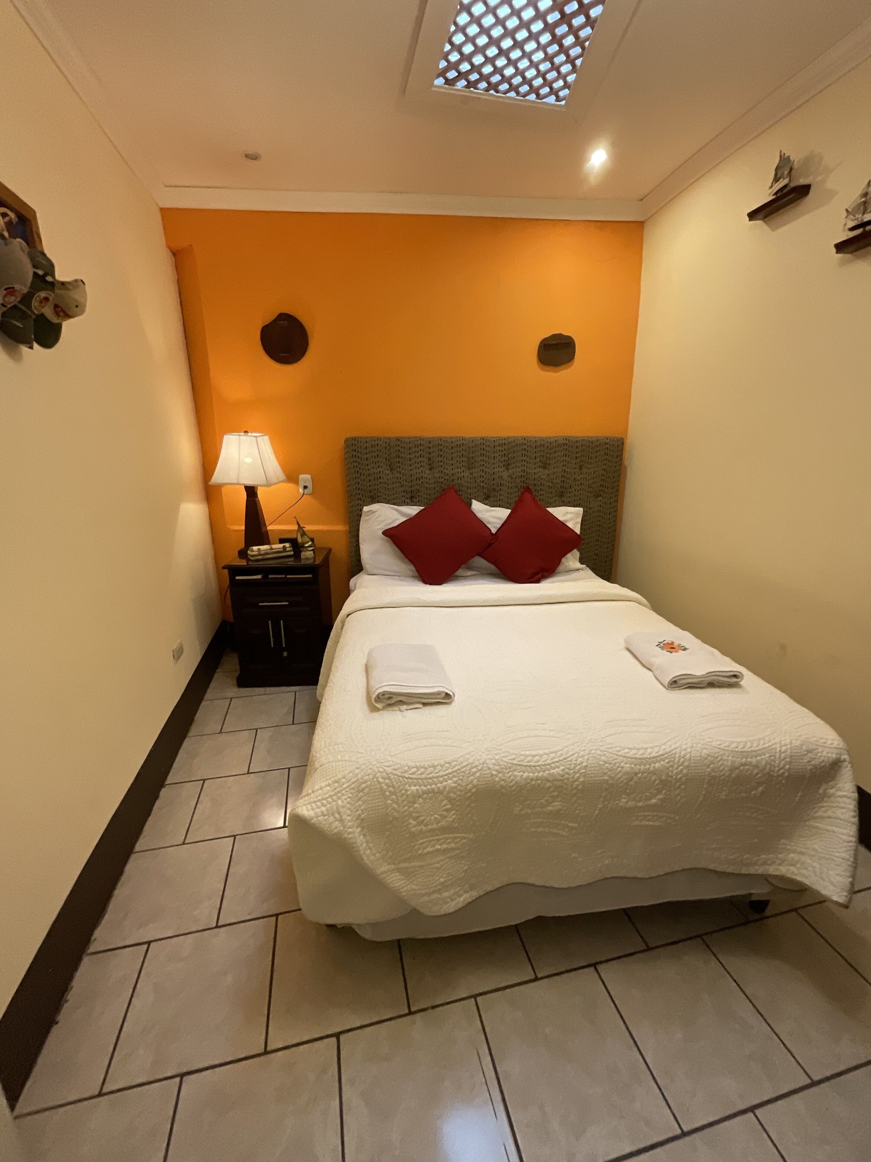 A hotel room with a bed, a nightstand, a lamp, and a small window.