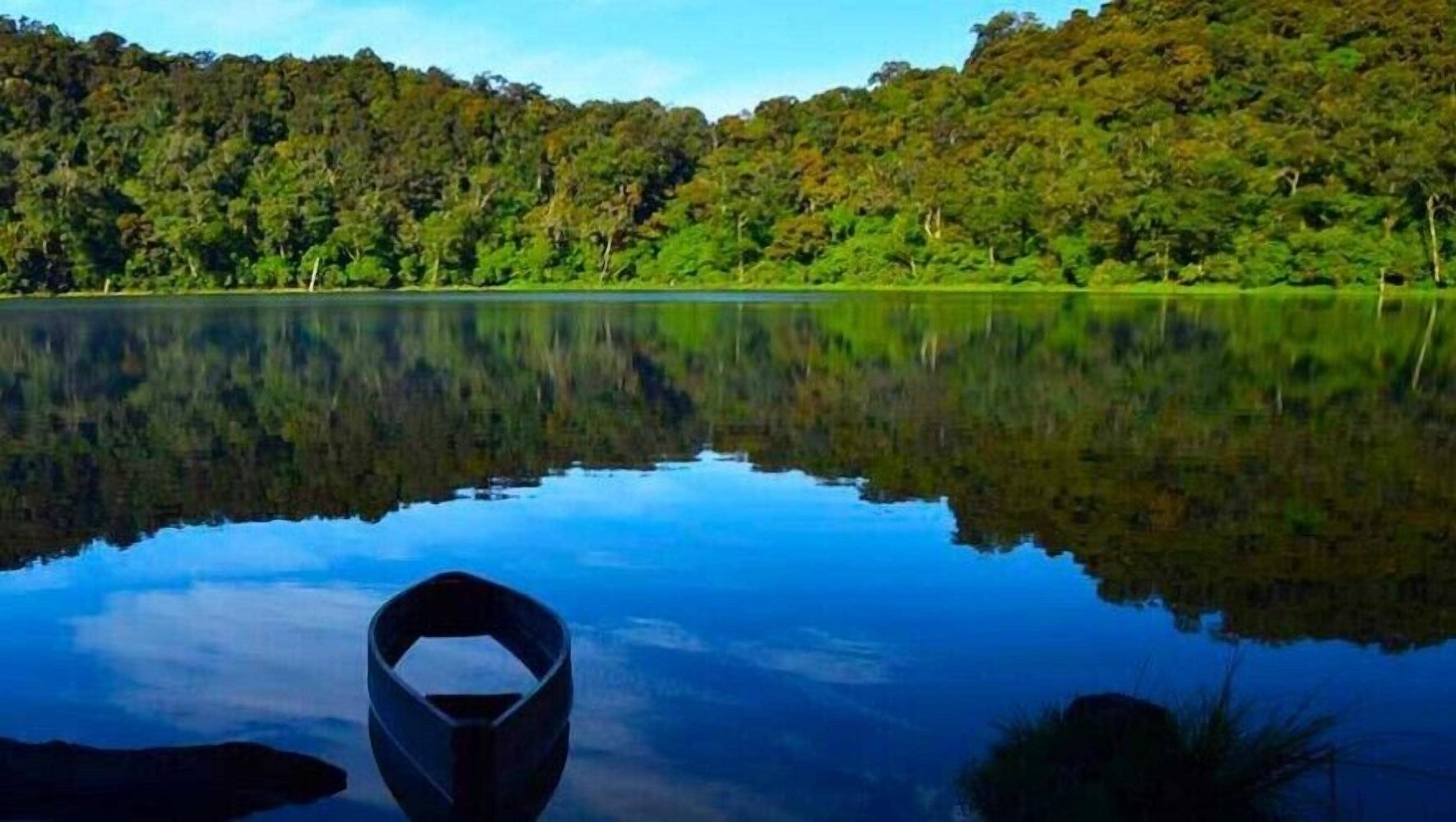 A calm lake with a boat in the foreground and dense forest in the background.