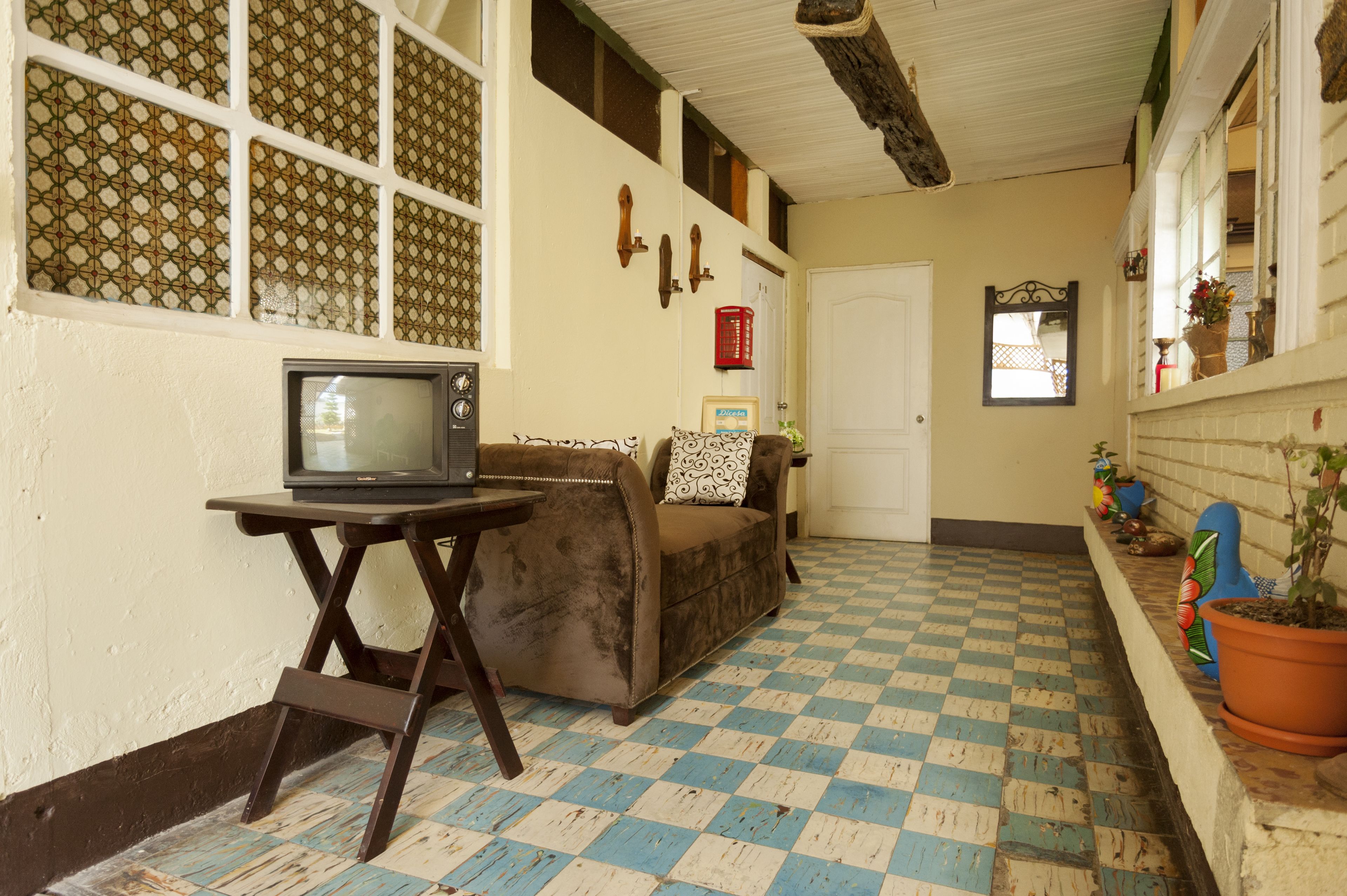Un pasillo con piso a cuadros, un sofá, un televisor sobre una mesa y una puerta.