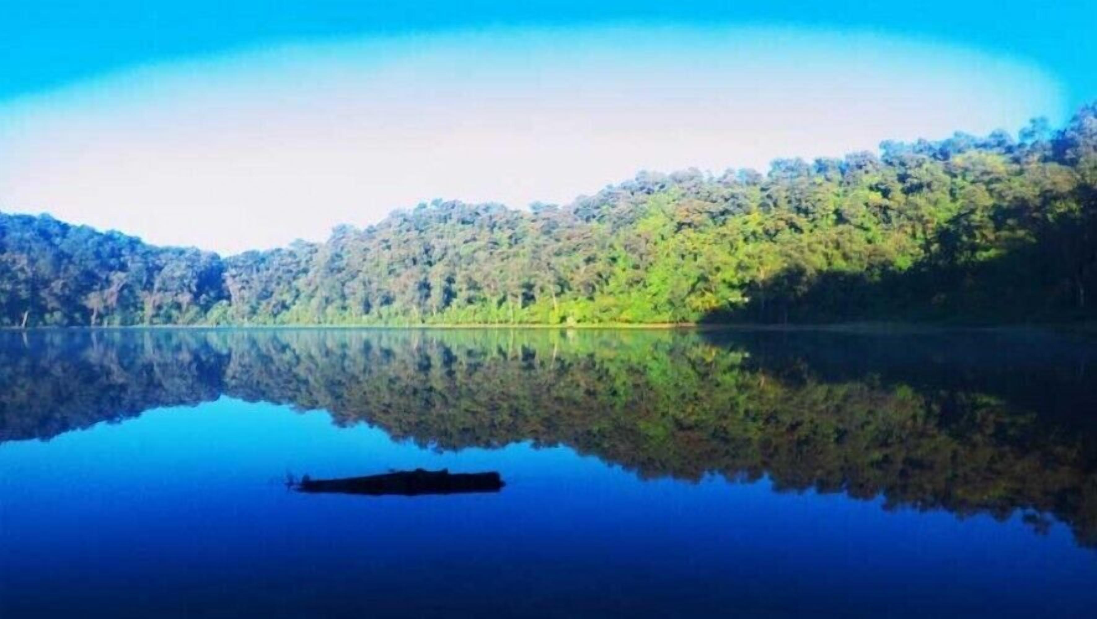 A calm lake with a boat in the foreground and dense forested hills in the background.