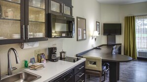 A compact kitchen with a sink, stove, and microwave. There is a dining area with a table and chairs. - Candlewood Suites Austin North by IHG (Austin)