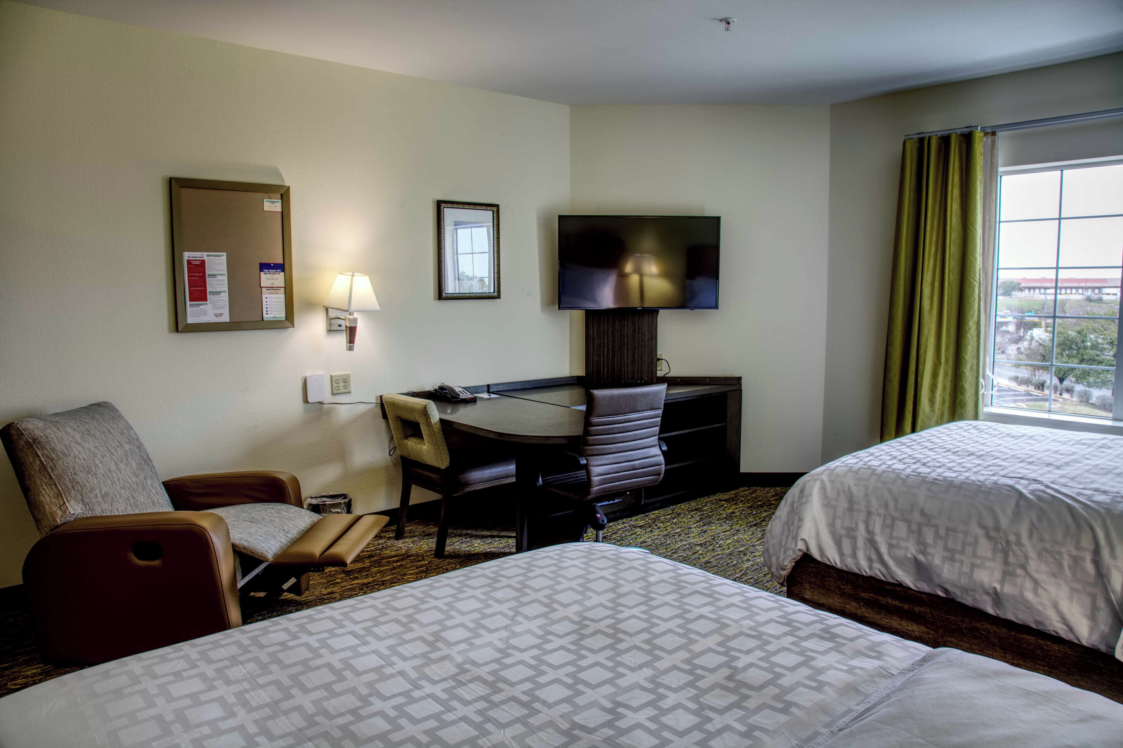 Une chambre d’hôtel avec deux lits, un bureau avec une chaise, une télévision et une fenêtre avec des rideaux.