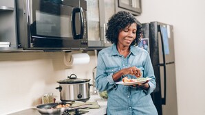 A kitchen with stainless steel appliances, a countertop with a pot and a pan, and a person holding a plate of food. - Candlewood Suites Austin North by IHG (Austin)